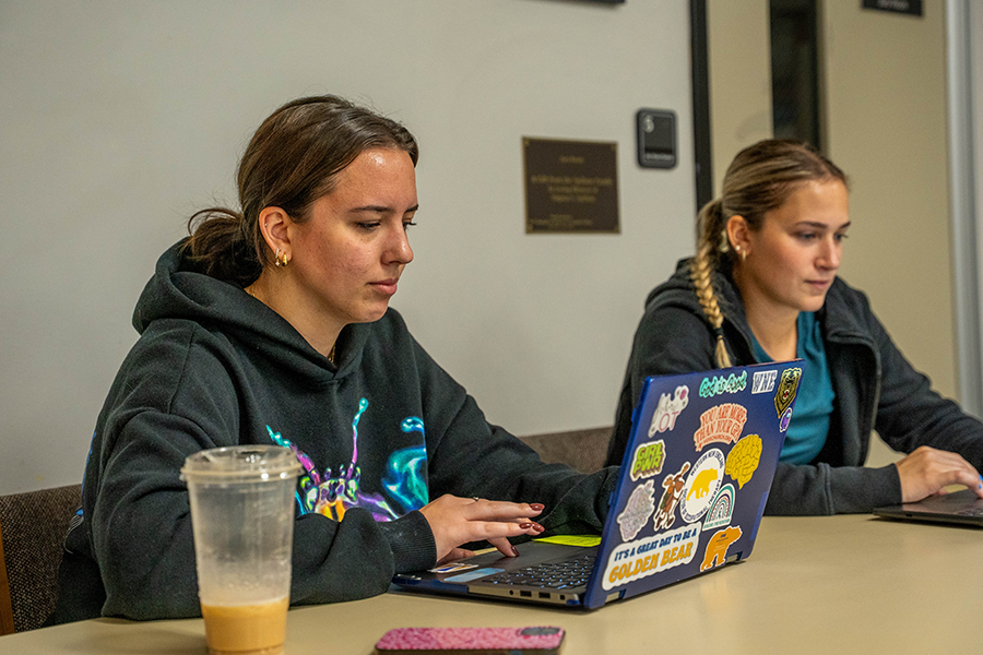 Two female students at a table with laptops