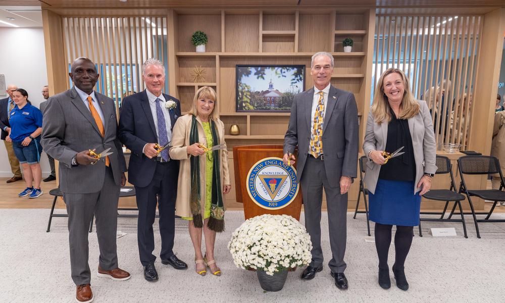 President Johnson, Kevin and Sandra Delbridge, Nick LaPier and Patty Goff hold gold scissors before the ribbon cutting while standing around a podium.