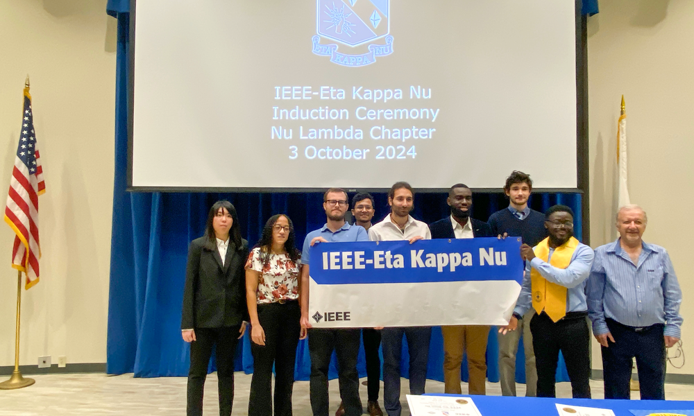 Eight students holding the IEEE-Eta Kappa Nu banner.