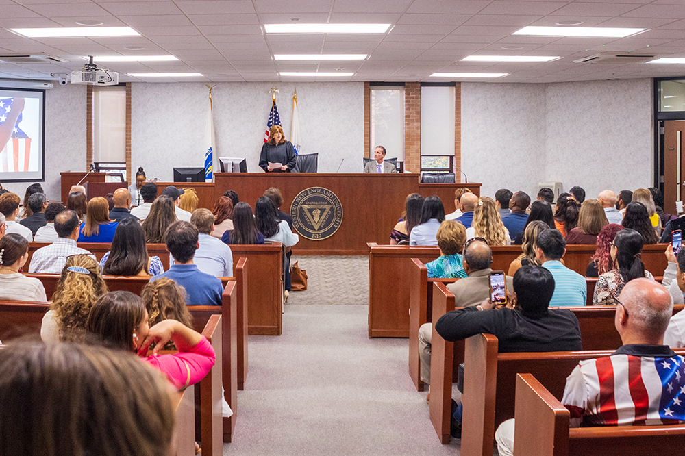 Broad photograph of the School of Law Moot Court with a federal judge presiding to deliver the Oath of Allegiance to 48 citizens.