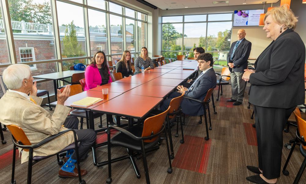 Students around a table talking with a business alumn.