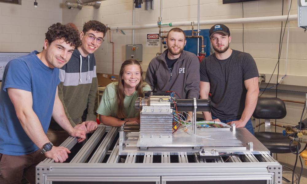 Five engineering students including one girl pose around a jet engine they designed