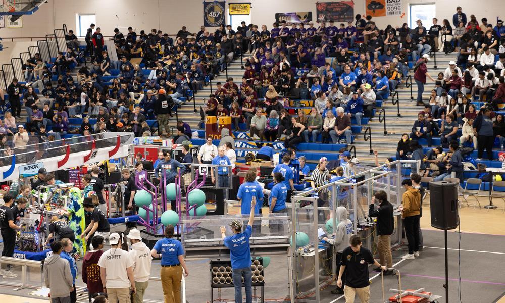 Wide shot of students with the robots surrounded on two sides by fans in the stands at WNE's gym.