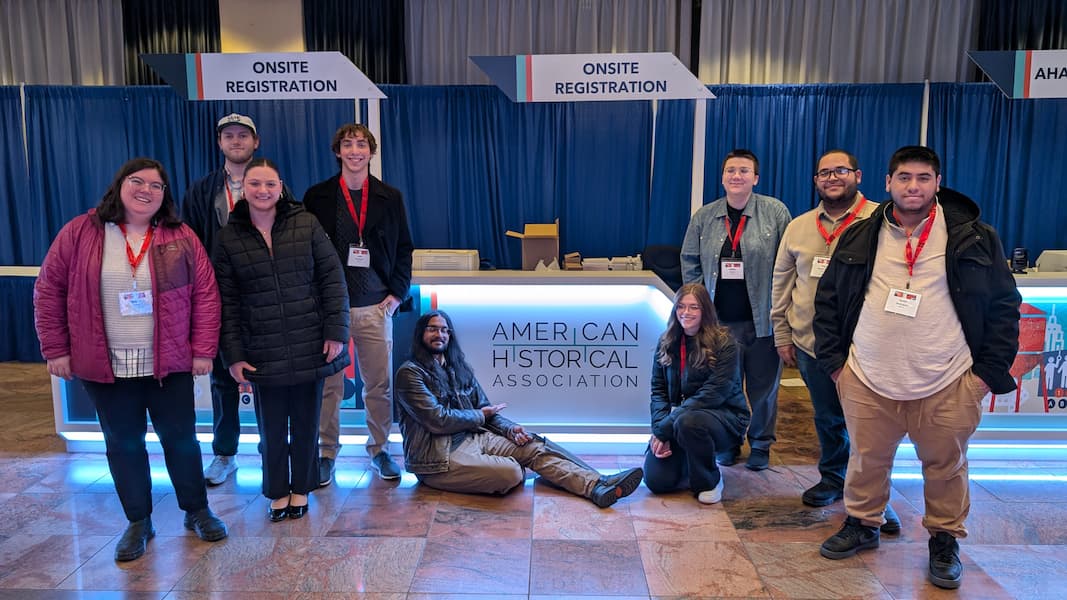 Nine history students pose around the registration table and the American History Association annual meeting