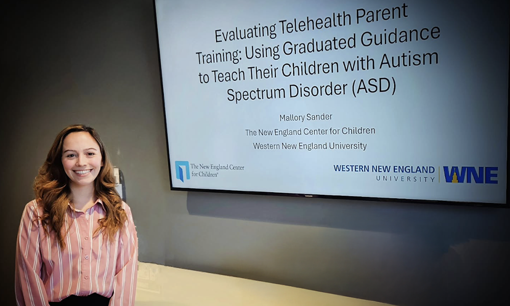 Student Mallory Sander stands in front of a powerpoint slide featuring the title of her research.
