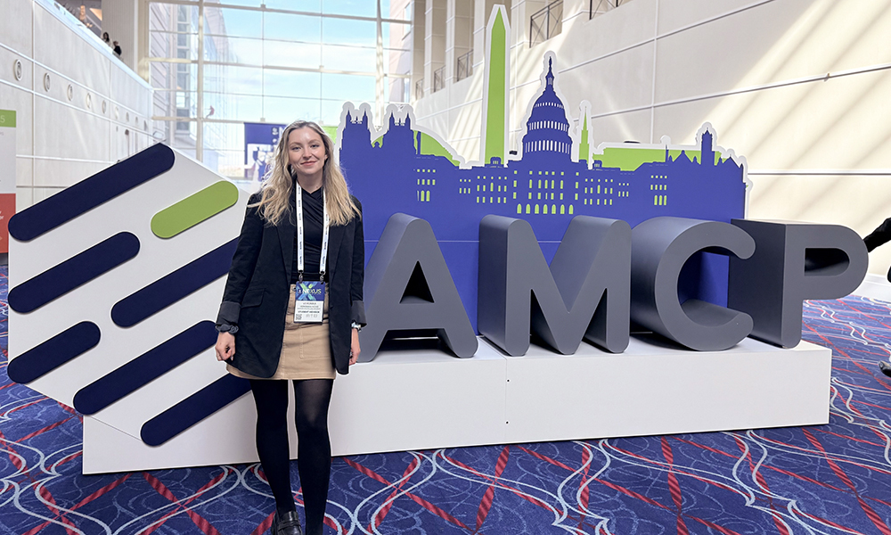 Student Veronika Hicks stands next to large graphic AMCP logo at a convention center