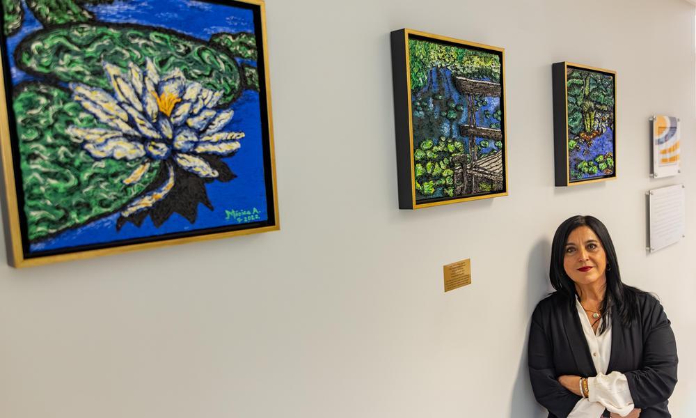 Monica Albarron stands under her three painting trilogy handing in the student hub
