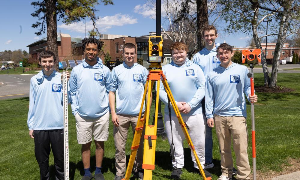 Six members of the surveying team in light blue shirts stand outside with surveying equipment.
