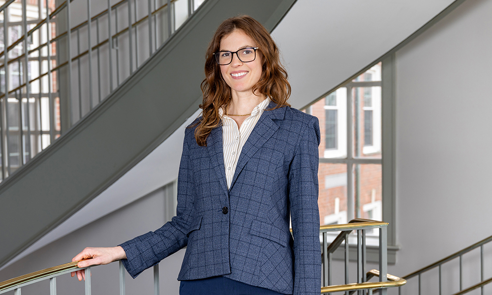 Sarah Morgan is standing at the top of a light filled stairwell with her hand one railing.