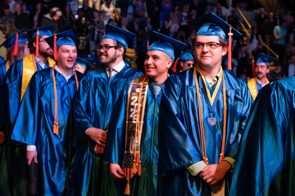 Four male undergraduates in blue robes take in the crowd at WNE Commencment 2026.
