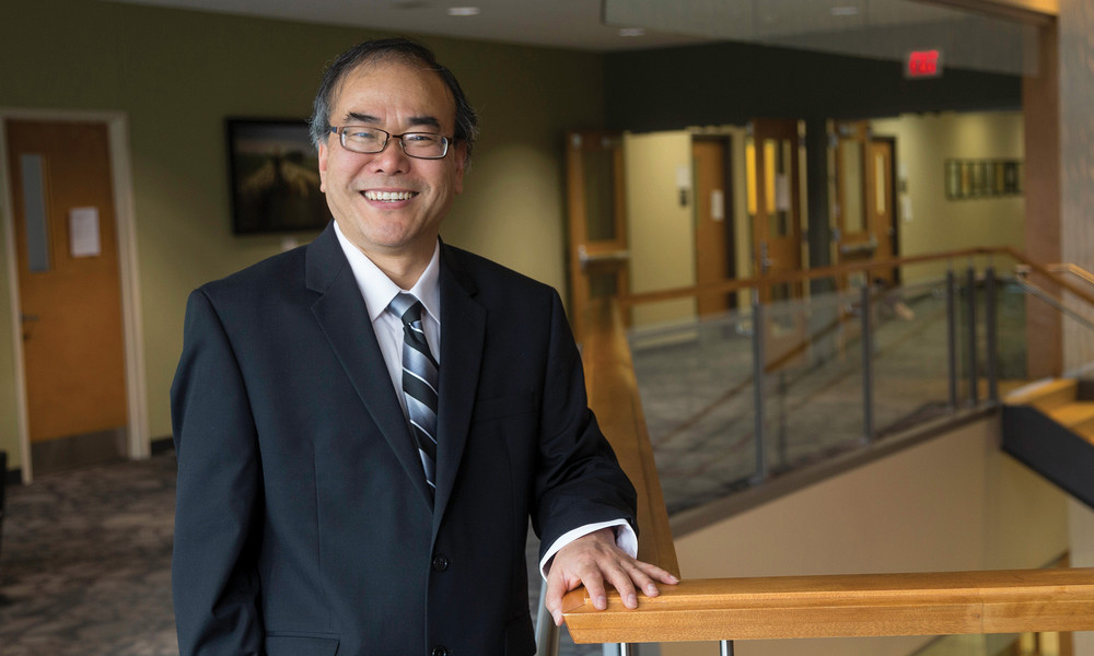 Professor Shusen Sun stands with hand on a stair railing smiling at camera.