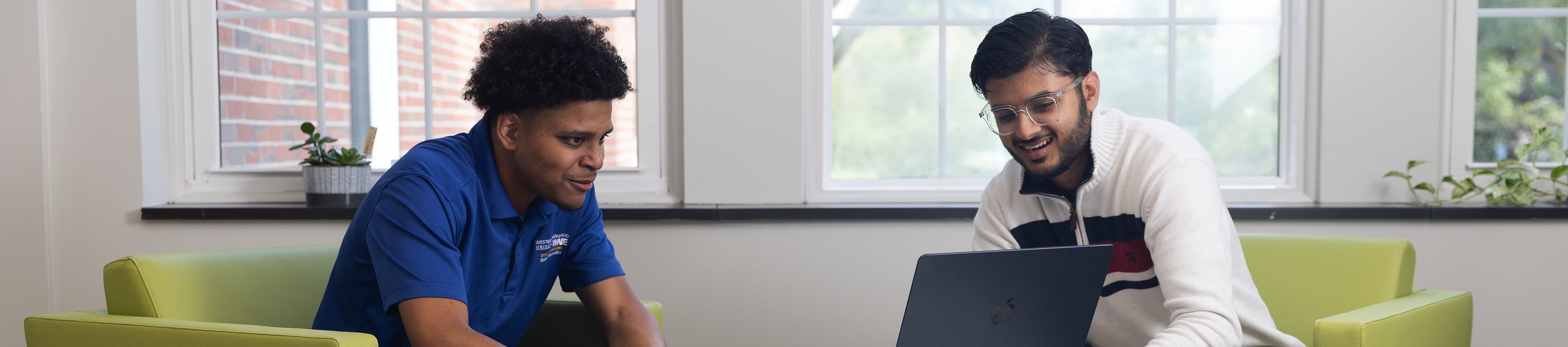 Two male students sitting together, one holding a laptop